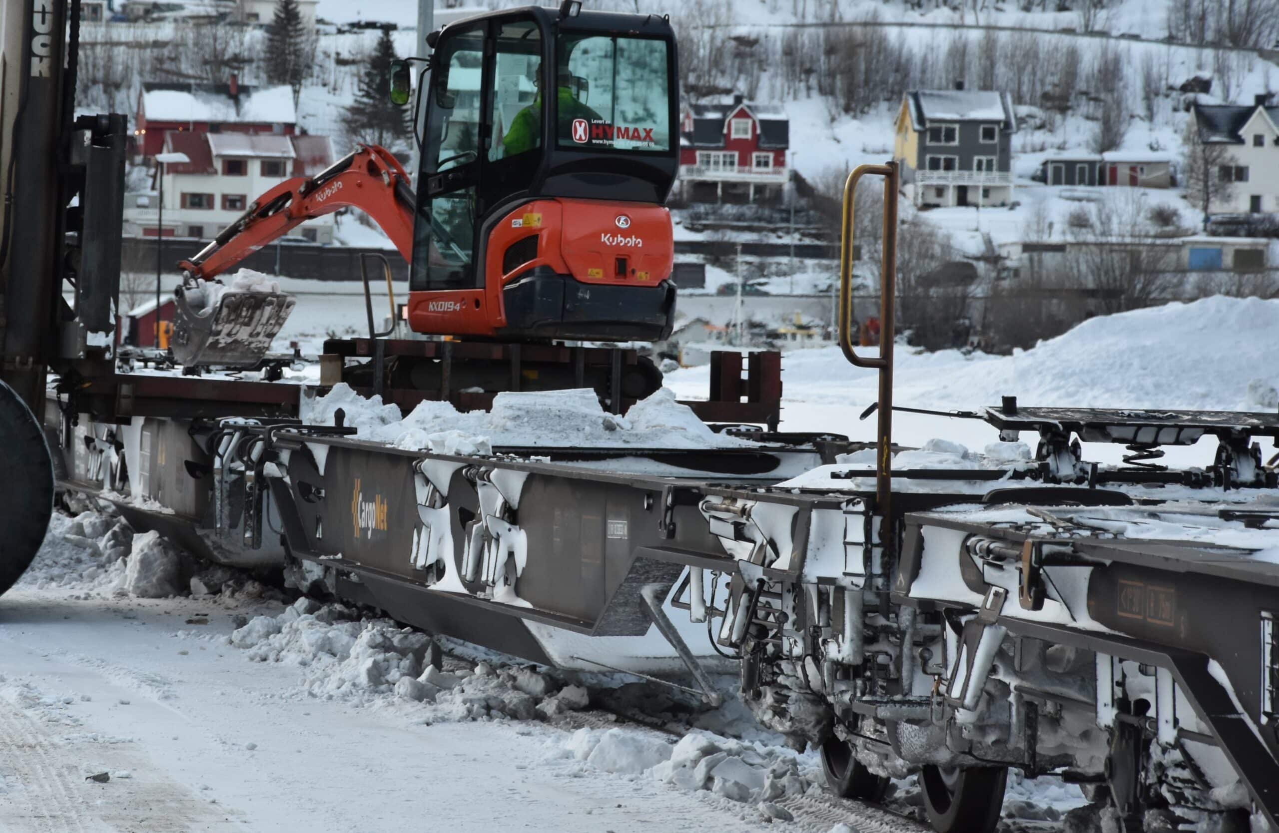 Snø og is i vognenes hjulbrønner fjernes med minigraver før ny opplasting kan skje. Her fra Narvik godsterminal.